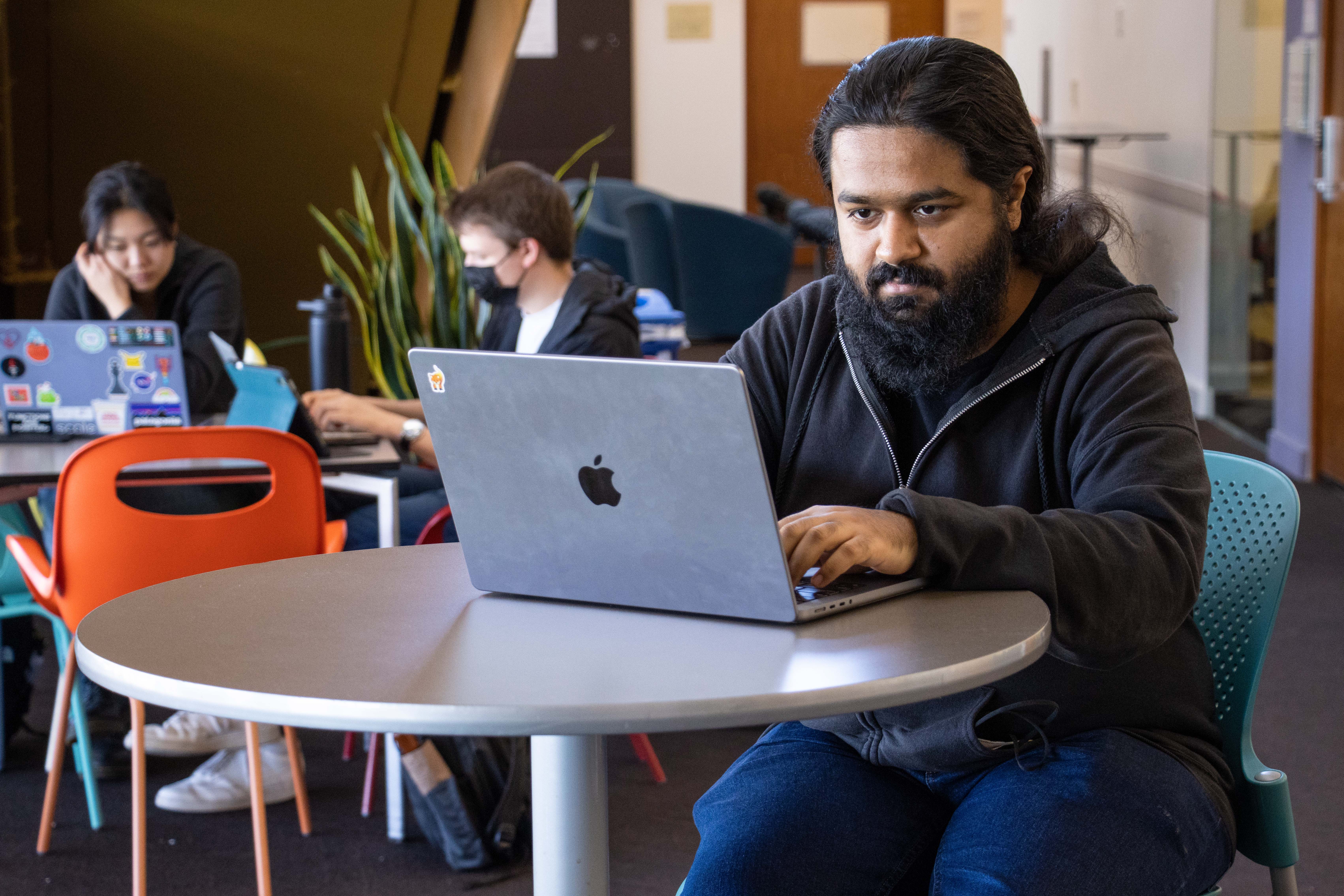 CSD doctoral student, Jay Bosamiya, at his laptop computer seated at a round table at Carnegie Mellon University