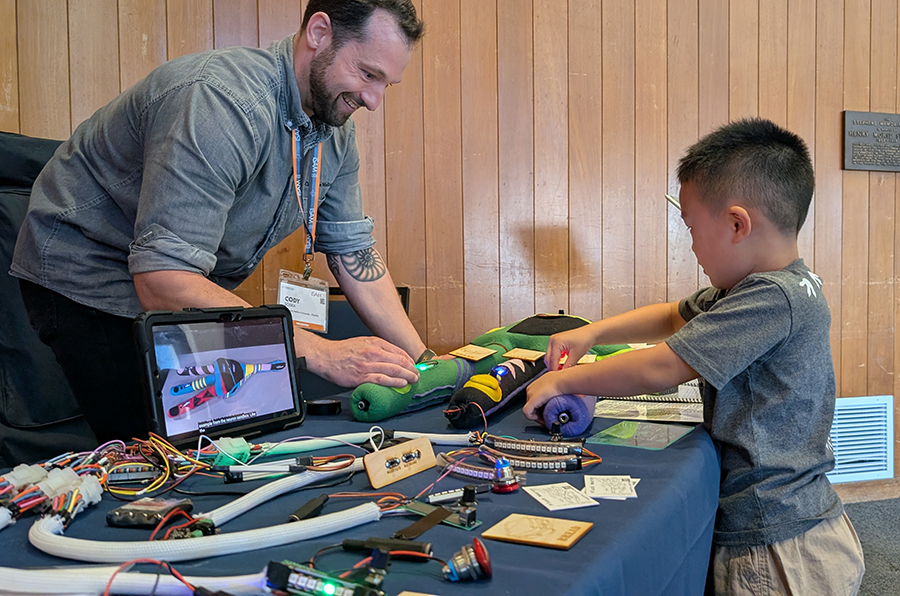 A man looks on as a child plays with a plush stuffie that resembles a neuron.